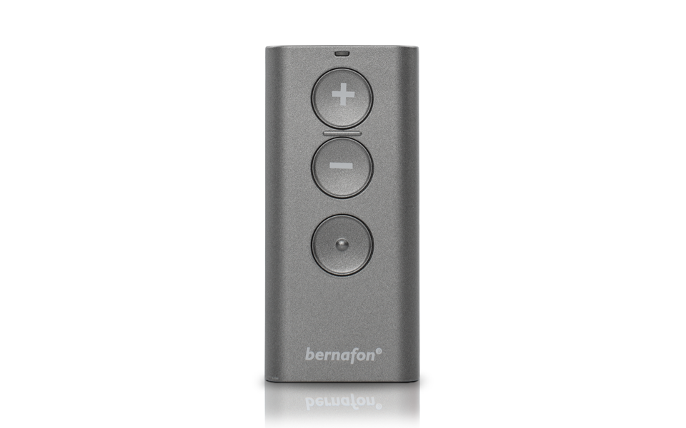 A compact, grey Bernafon RC-A Remote with three circular buttons (plus, minus, and center) rests on a white background. The Bernafon logo appears at the bottom of the device.