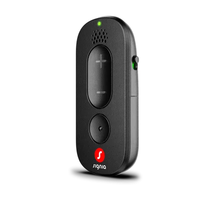 A compact Signia Remote Control in black, equipped with volume buttons, a prominent central button, a speaker grille, and a glowing green indicator on the side, standing upright against a light gray background.